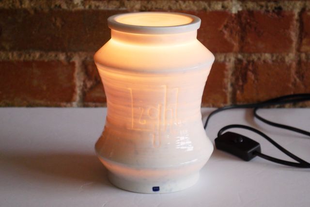 Porcelain jar glowing warmly from the inside through textured walls and a porcelain lid. The word light has been carved in a playful slab serif handwriting, and glows extra bright.
