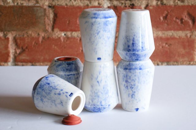 Six stacked salt and pepper shakers in a glossy white finish with a splash of blue.
