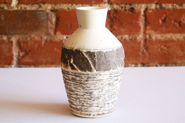 Bottle vase in organic sepia-like matte finish. The narrow base has a small vertical ring, before angling out in deep textured grooves that capture the toasty colors in relief - white highlights, and sepia grooves.
