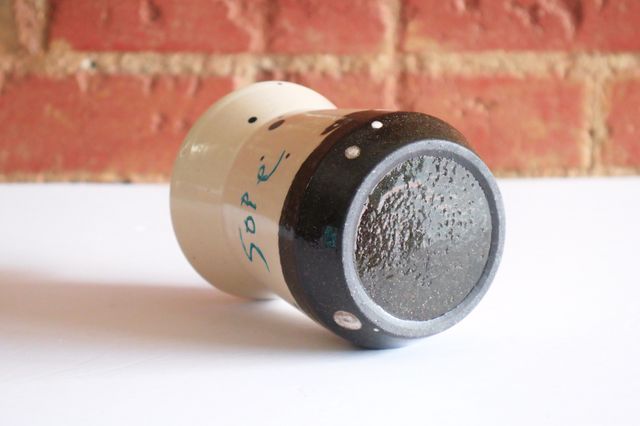 The base is inset, with a slight outer ring. There are white circles of various sizes painted on the black clay.
