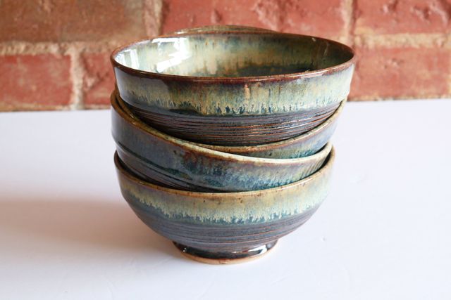 Four bowls stacked slightly askew. They have a glossy organic finish, which whites and blues flowing over a dark translucent red-brown – almost like an iris, or nebula.
