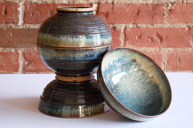 Three of the bowls are stacked foot-to-foot and rim-to-rim, highlighting the nearly-uniform size of each. My small-m stamp is visible on the bare underside of each angular foot-ring. A fourth is bowl is leaning outward to display the flowing blues with organic splashes of white breaking red-brown over the rim.
