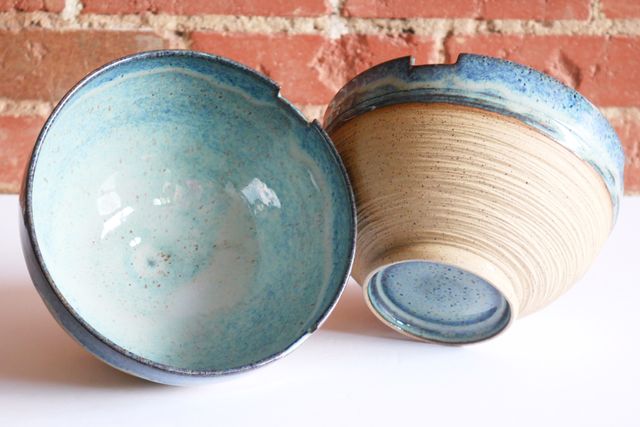 One bowl tilted towards camera, showing the glazed insides - darker blue at the rim and gathering into lighter blues towards the base. The other bowl tilts away, revealing the same blue glaze hidden inside the half-inch deep angled foot ring.
