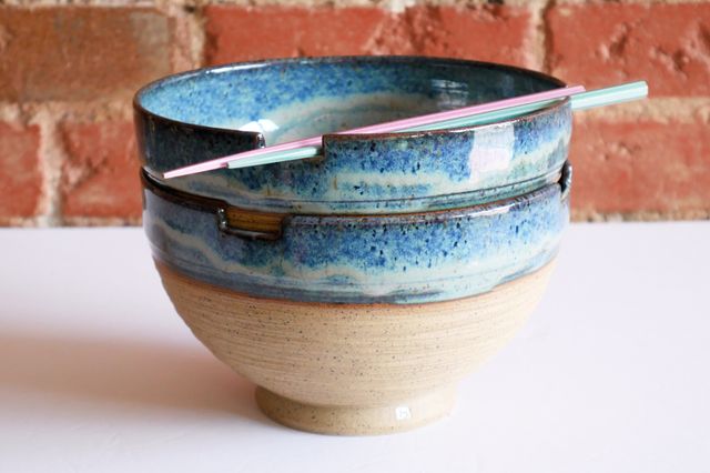 Two large bowls stacked neatly, with chopsticks resting across notches in the rim of the top bowl. Most of the bowl is raw speckled light brown clay with deep grooved rings of texture, while the inside and top inch or so are smooth and glazed in a floating blue that gathers organically in lighter and darker patches.

