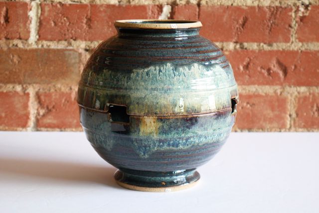 One bowl is inverted, sitting rim-to-rim on the other. The rim diameters and placement of the notches match very closely. Both bowls have an inch-plus smooth rim, and then texture carved in overlapping rings down to the foot which is also smooth. The glaze pools in floating blues inside the texture, while breaking deep red brown over the high points. There's a blue-and-white nebula cloud dripping from the rim.
