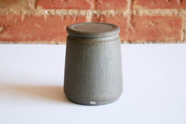 With the lid on, the jar has clean lines -- pushing out slightly at the base, and then angling gently back in to an inset lip. The clay is raw with a slightly rough texture, but straight lines, gray with areas of toasty brown.
