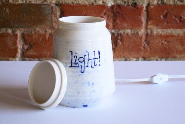 Hand-lettering says light! in a playful slab serif inlaid with blue. There's also a light splatter of blue across the front. The lid has a thick rim, and slightly inset top, with a locating flange underneath.