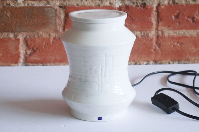 With the light off, the jar is white with a blue stamp at the base and a subtle blue splatter. The carved lettering is even more subtle now, combining with the textured rings of the piece.
