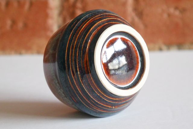 The underside has an outset white clay foot ring with glaze inside and around. the lower angle of the cup has a grooved texture, while the upper angle is smooth.
