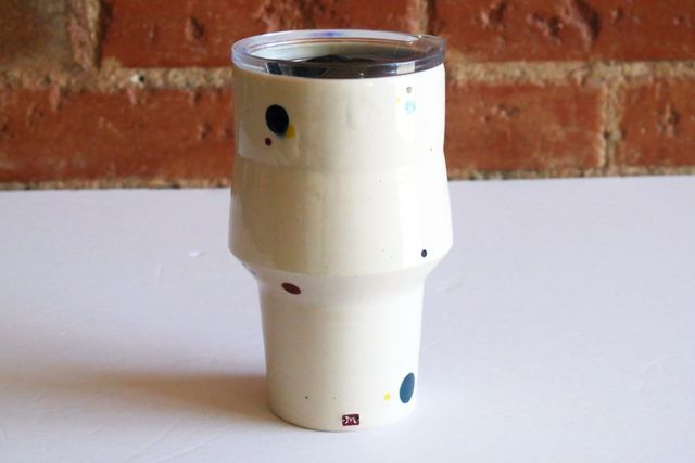 Angular White tumbler with a narrow cup-holder-friendly base that flares slightly in the first couple inches, and then angles out more dramatically, and slopes gently back in towards the vertical lip. A travel lid fits snug at the top.