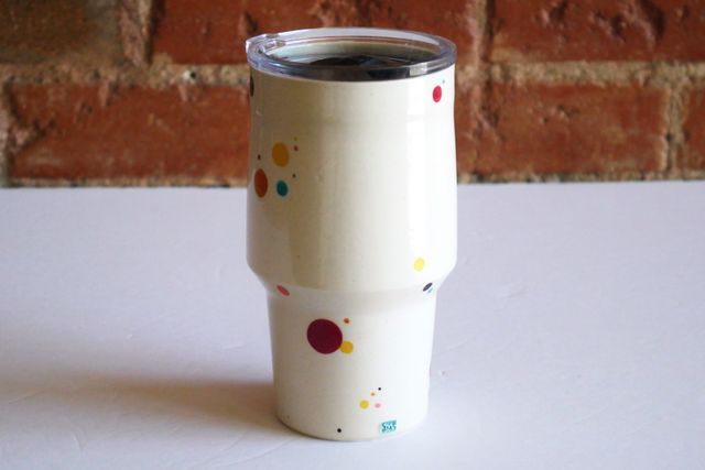Angular White tumbler with a narrow cup-holder-friendly base that flares slightly in the first couple inches, and then angles out more dramatically, and slopes gently back in towards the vertical lip. A travel lid fits snug at the top.
